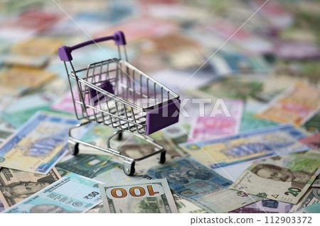 Supermarket trolley on many banknotes of different currency. Background of shopping worldwide close up Supermarket trolley on many banknotes of different currency. Background of shopping worldwide close up 112903372