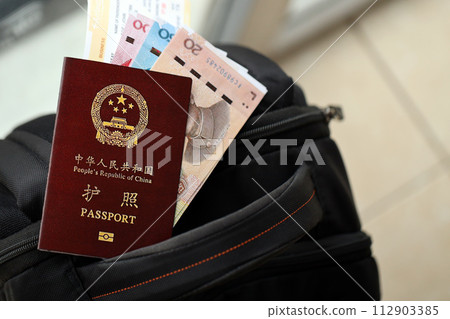 Red passport of People Republic of China and chinese yuan money bills with airline tickets on backpack close up. PRC passport 112903385