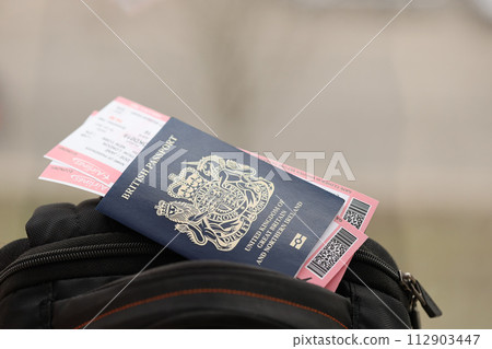 Blue British passport with airline tickets on touristic backpack close up. Tourism and travel concept 112903447