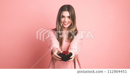Happy female model giving gift box against pink background Happy female model giving gift box against pink background 112904451