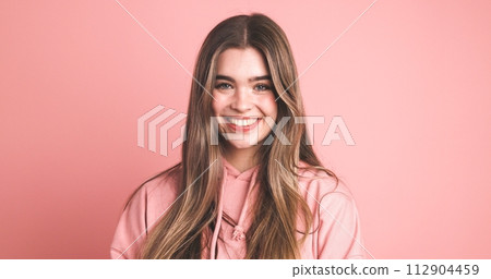 Happy female model in pink hoodie smiling over pink background Happy female model in pink hoodie smiling over pink background 112904459
