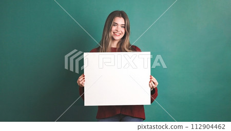 Happy woman holding blank white placard for advertisement purpose against green background 112904462
