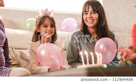 Girl blowing out the candles on her birthday cake sitting on a sofa 112904489