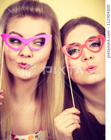 Two happy women holding fake eyeglasses on stick Two happy women holding fake eyeglasses on stick 112904800
