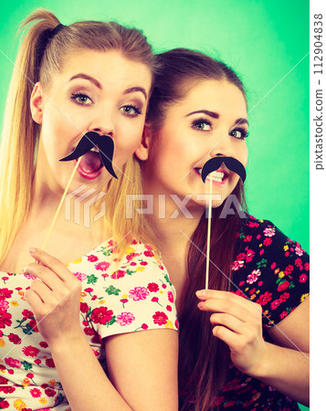 Two happy women holding fake moustache on stick Two happy women holding fake moustache on stick 112904838