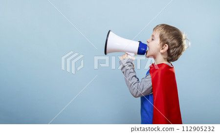 Child in superhero costume using megaphone. Blue background with copy space Child in superhero costume using megaphone. Blue background with copy space 112905232