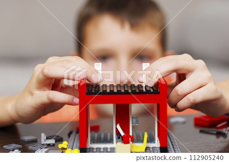 Child building a red toy structure with blocks on a table Child building a red toy structure with blocks on a table 112905240