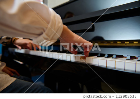 Musician pianist puts fingers on piano keys, playing piano, enjoying performance of classical melody during music lesson Musician pianist puts fingers on piano keys, playing piano, enjoying performance of classical melody during music lesson 112905535