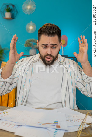 Frustrated upset angry businessman works with paperwork reports documents on laptop at home office Frustrated upset angry businessman works with paperwork reports documents on laptop at home office 112906524