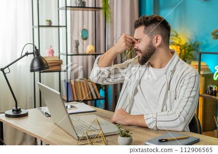 Bored sleepy businessman worker working on laptop rubbing eye pinch nose, pain headache at office 112906565