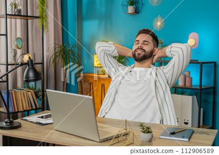 Man sitting at table after finishing online distant work on laptop pc at home office room Man sitting at table after finishing online distant work on laptop pc at home office room 112906589