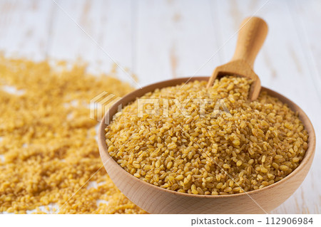 Organic dry bulgur are scattered in a wooden bowl close up. Organic dry bulgur are scattered in a wooden bowl close up. 112906984