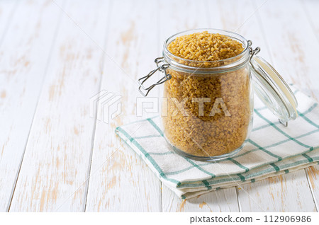 Raw bulgur in glass storage jar on a white wooden table. Raw bulgur in glass storage jar on a white wooden table. 112906986