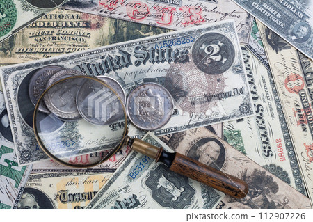 Old US banknotes and silver certificates with silver dollar coins and magnifying glass Old US banknotes and silver certificates with silver dollar coins and magnifying glass 112907226
