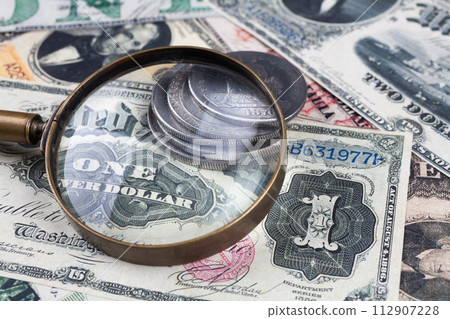 Old US banknotes and silver certificates with silver dollar coins and magnifying glass 112907228