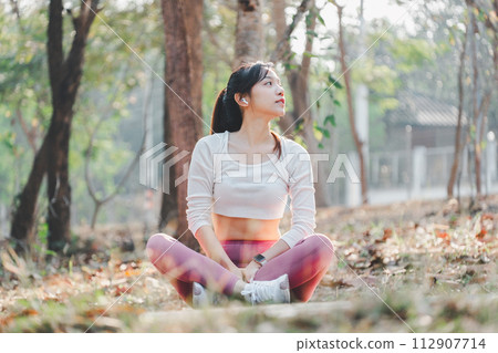 Woman sitting cross legged in a park, looking up thoughtfully after a refreshing outdoor workout session. Woman sitting cross legged in a park, looking up thoughtfully after a refreshing outdoor workout session. 112907714