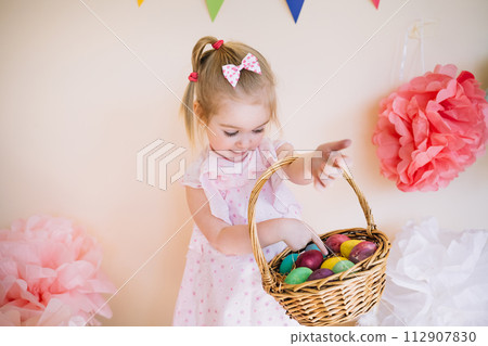Cute little girl wearing pink dress holding basket with painted Easter eggs Cute little girl wearing pink dress holding basket with painted Easter eggs 112907830