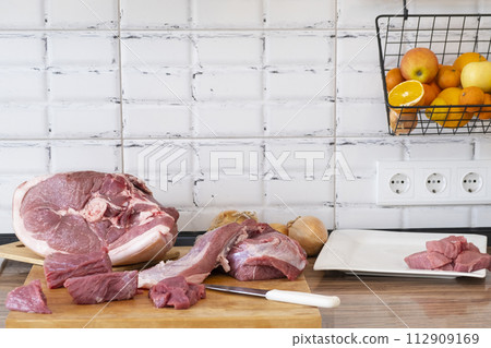 Different tipes of meat, cutting fresh raw meat on board in white kitchen. Preparing pork meat, cooking Different tipes of meat, cutting fresh raw meat on board in white kitchen. Preparing pork meat, cooking 112909169