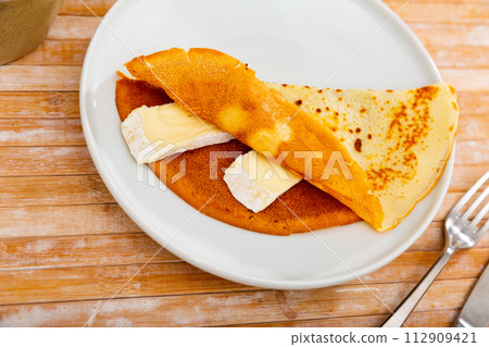 On plate - ruddy soft pancakes with pieces of tender cream brie cheese 112909421