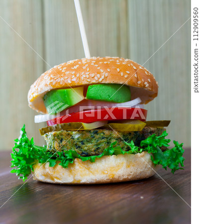 Vegetarian hamburger with soybean patty, fresh vegetables and avocado at plate Vegetarian hamburger with soybean patty, fresh vegetables and avocado at plate 112909560