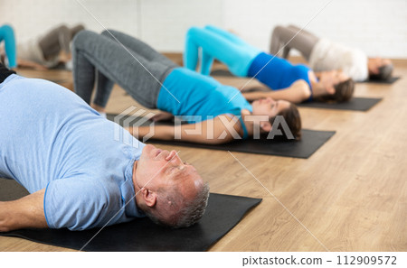 Aged man performing glute bridge in fitness studio 112909572