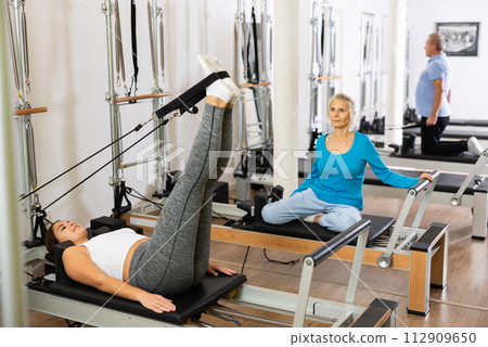 Relaxed young woman doing exercise for lower back on Pilates chair equipment during workout in rehabilitation center Relaxed young woman doing exercise for lower back on Pilates chair equipment during workout in rehabilitation center 112909650