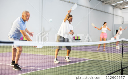 Senior man playing doubles pickleball with male partner indoors 112909657