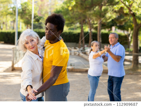 Carefree senior multiracial couples dancing in pairs outdoors during sunny day at park Carefree senior multiracial couples dancing in pairs outdoors during sunny day at park 112909687