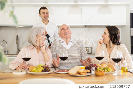 Mature married couple are sitting at table, enjoying food and wine with middle-aged guests. Mature married couple are sitting at table, enjoying food and wine with middle-aged guests. 112909797