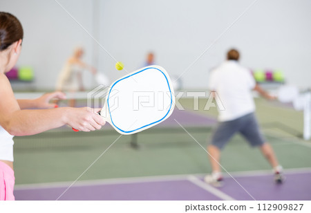Paddle-shaped racquet for pickleball in hand of female player 112909827
