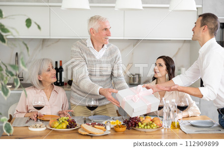 Birthday senior man accepts outright gift and greetings from adult son during family feast 112909899