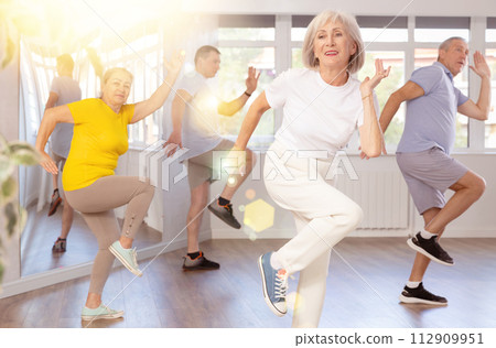 Cheerful elderly woman learning dynamic dances at group choreography lesson Cheerful elderly woman learning dynamic dances at group choreography lesson 112909951