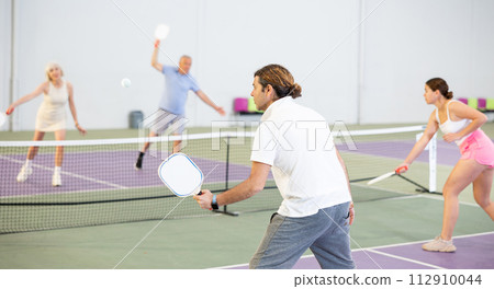 Rear view of adult man playing pickleball on indoor court Rear view of adult man playing pickleball on indoor court 112910044
