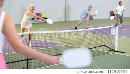 Sporty senior woman playing pickleball on indoor court 112910064