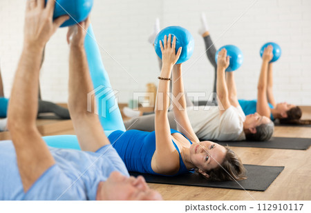 Middle-aged woman practicing pilates with ball in gym area 112910117