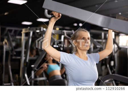 Older sportswoman training at shoulder press machine in gym Older sportswoman training at shoulder press machine in gym 112910266