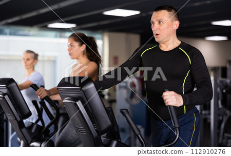 Middle aged man in the gym is engaged in sports using an ellipsoid simulator. Healthy lifestyle and sport concept Middle aged man in the gym is engaged in sports using an ellipsoid simulator. Healthy lifestyle and sport concept 112910276