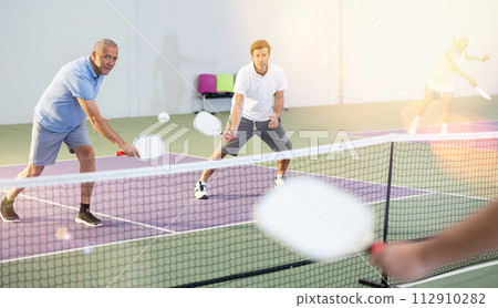 Aged man playing doubles pickleball match with male partner Aged man playing doubles pickleball match with male partner 112910282