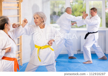 Old woman attendee of karate classes fighting with her opponent in sports hall Old woman attendee of karate classes fighting with her opponent in sports hall 112910287