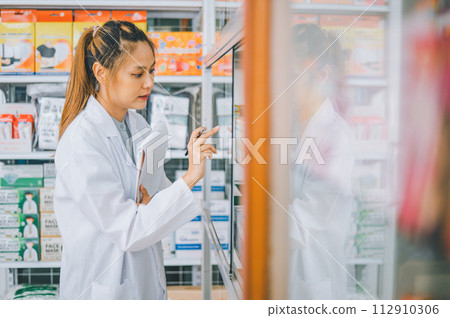 Pharmacist checking Checks Inventory of Medicine, Drugs, Vitamins with tablet and checking patient's prescription in modern pharmacy. 112910306