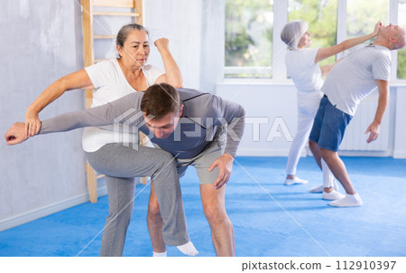 Senior woman in pair with middle-aged coach train Krav Maga and self-defense skills. 112910397