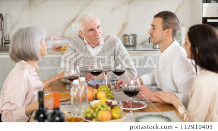 Mature married couple are sitting at table, enjoying food and wine with middle-aged guests. 112910403
