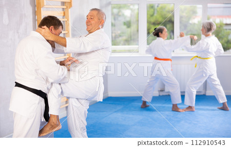 Old man attendee of karate classes fighting with his opponent in sports hall 112910543