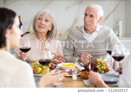 Senior parents sitting at table drinking wine and having conversation with young couple 112910557