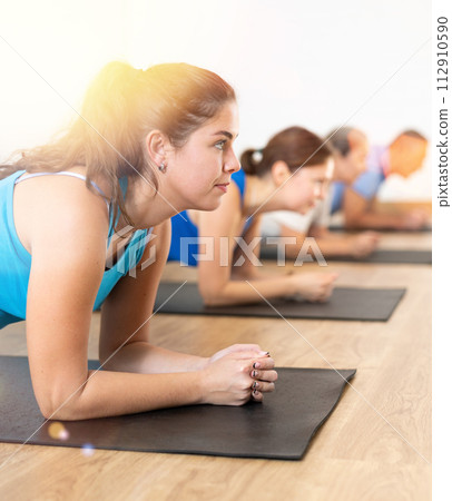 Class of male and women of different ages standing in plank on elbows during Pilates training together in gym Class of male and women of different ages standing in plank on elbows during Pilates training together in gym 112910590