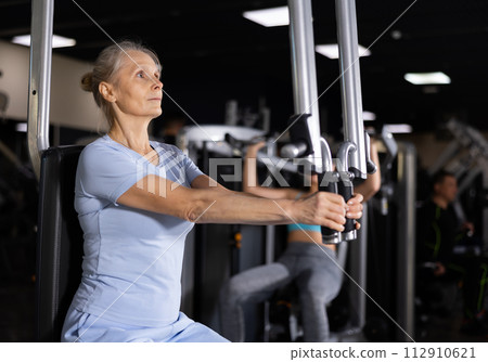 Portrait of elderly woman during workout with power exercise machine in gym Portrait of elderly woman during workout with power exercise machine in gym 112910621