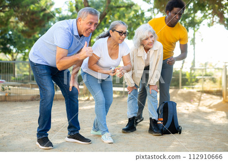 Positive multiracial mature people playing petanque game outdoors in autumn 112910666