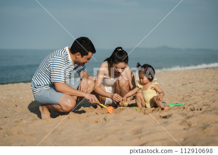 toddler baby girl playing sand toy with father and mother. happy family on the sea beach 112910698