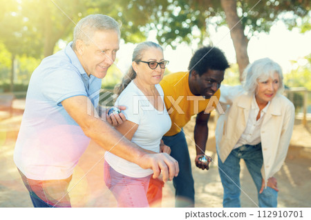 Cheerful males and females playing petanque in park on holidays Cheerful males and females playing petanque in park on holidays 112910701