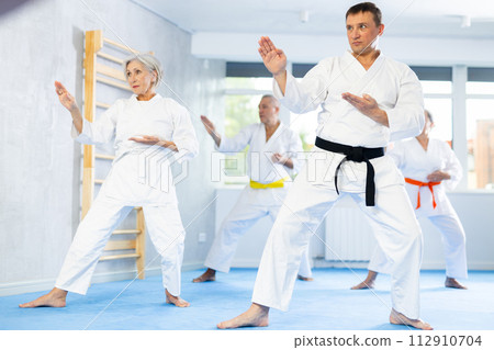 Group of mature people in kimono trying new fighting techniques at karate lessons Group of mature people in kimono trying new fighting techniques at karate lessons 112910704
